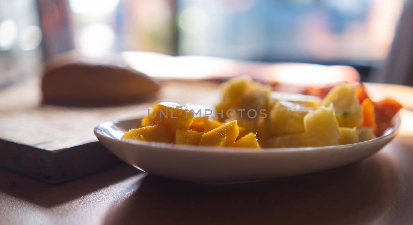 White plate of mango, pineapple, and papaya slices on table with blurry and bright background. Tasty and fresh sliced fruit on an oval porcelain plate. Healthy food and breakfast