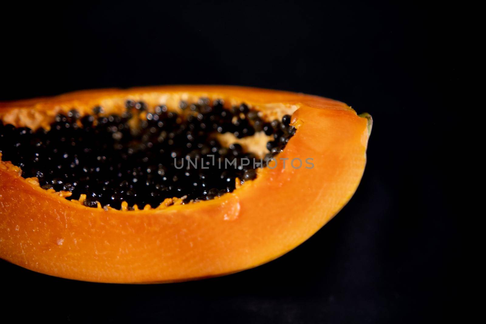 Half of fresh papaya laying down on black surface by Kanelbulle