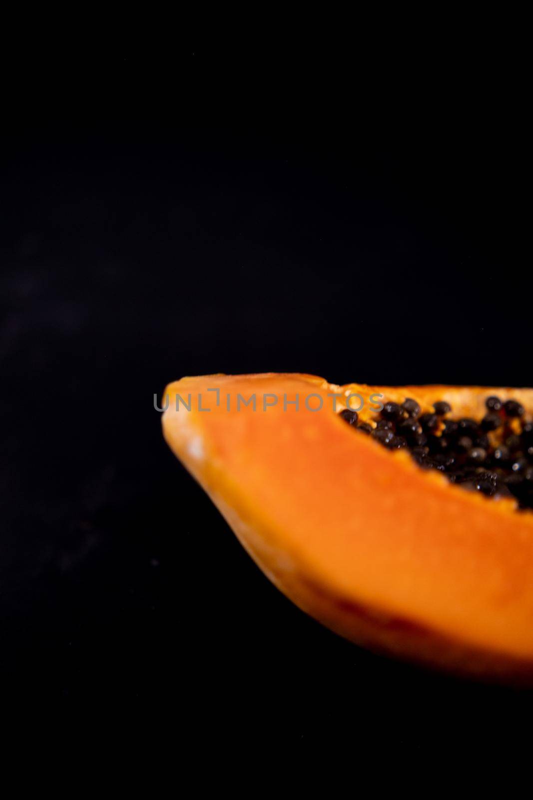 Half of fresh papaya laying down on black surface by Kanelbulle
