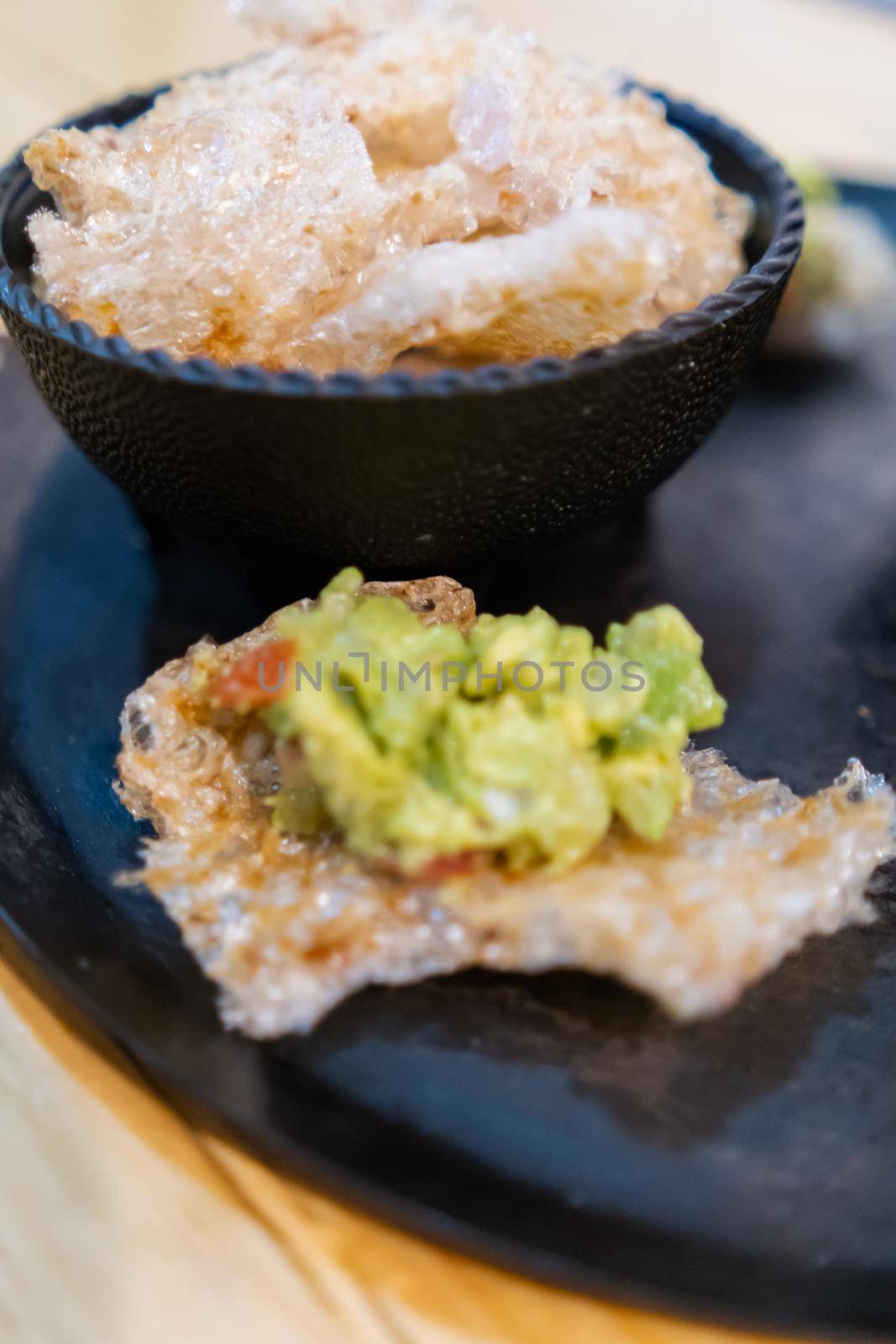 Pork rind with guacamole and bowl of pork rinds on traditional Mexican comal by Kanelbulle