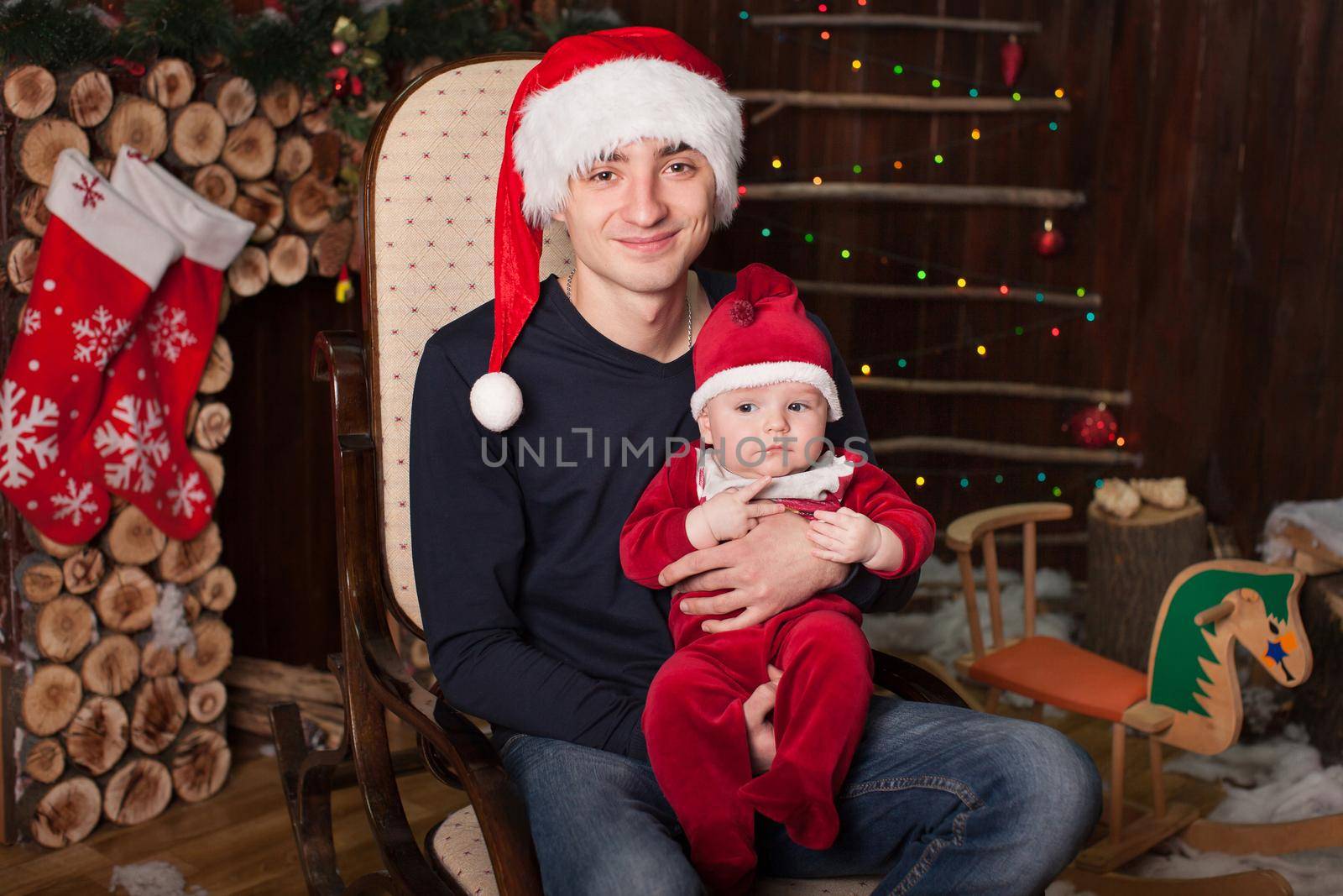 A man with a child dressed as Santa Claus on an armchair by a wooden fireplace on New Year's Eve