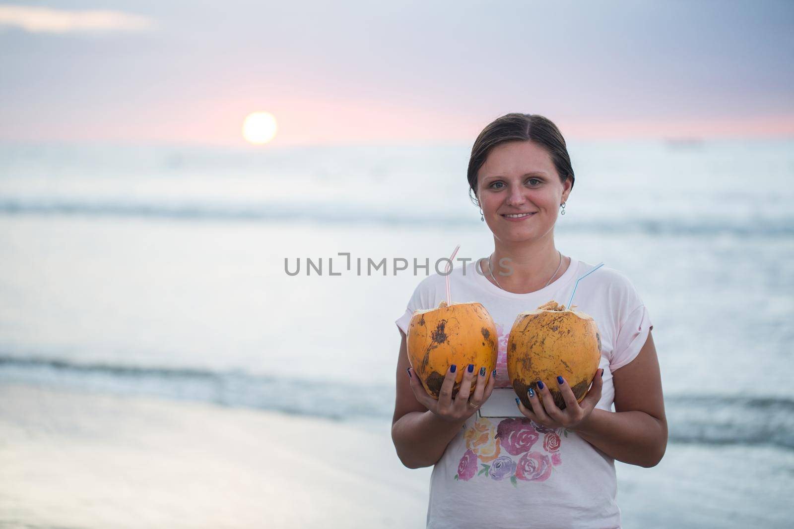 Young beautiful woman with coconuts at sunset.
