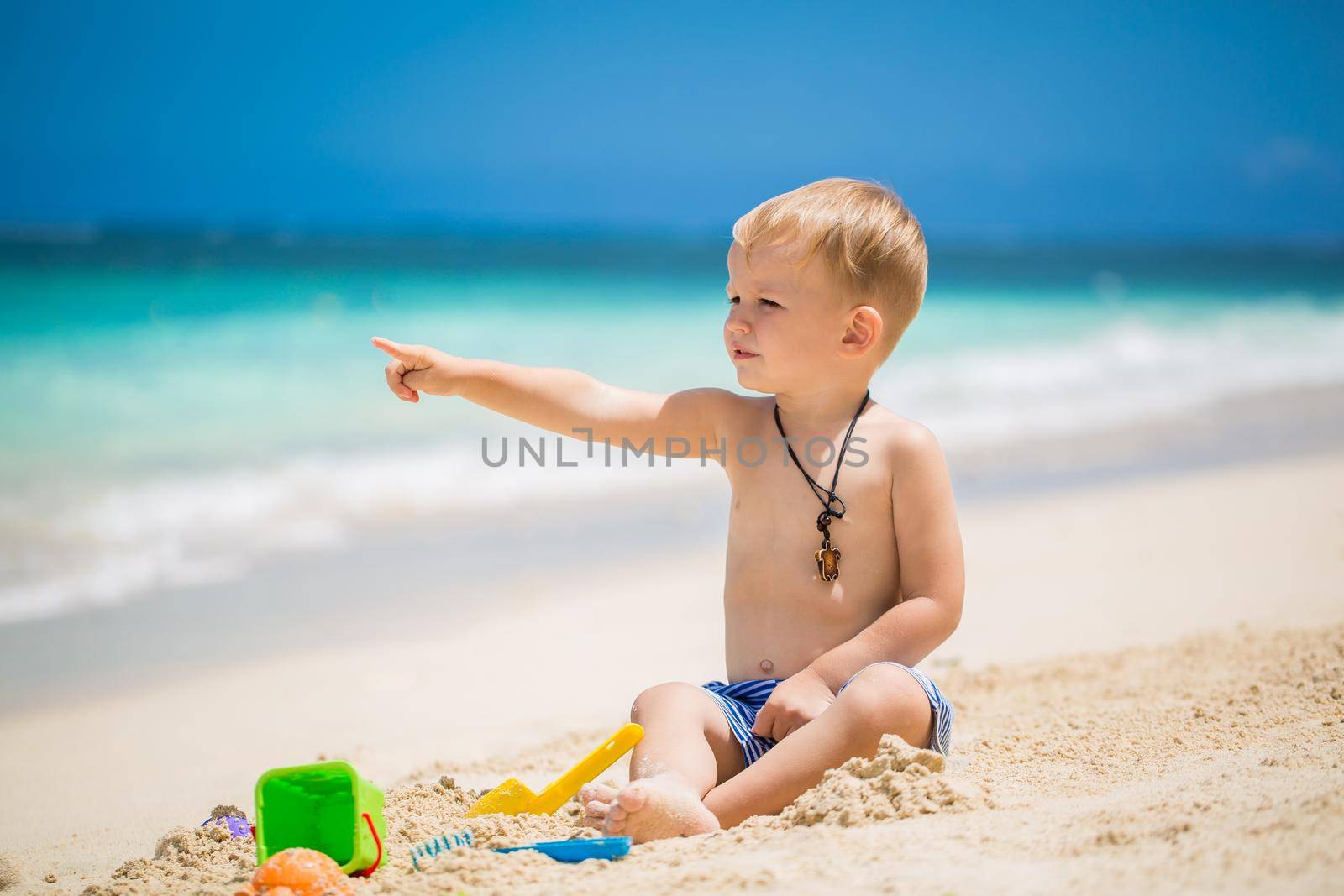 Cute baby boy playing with beach toys on tropical beach