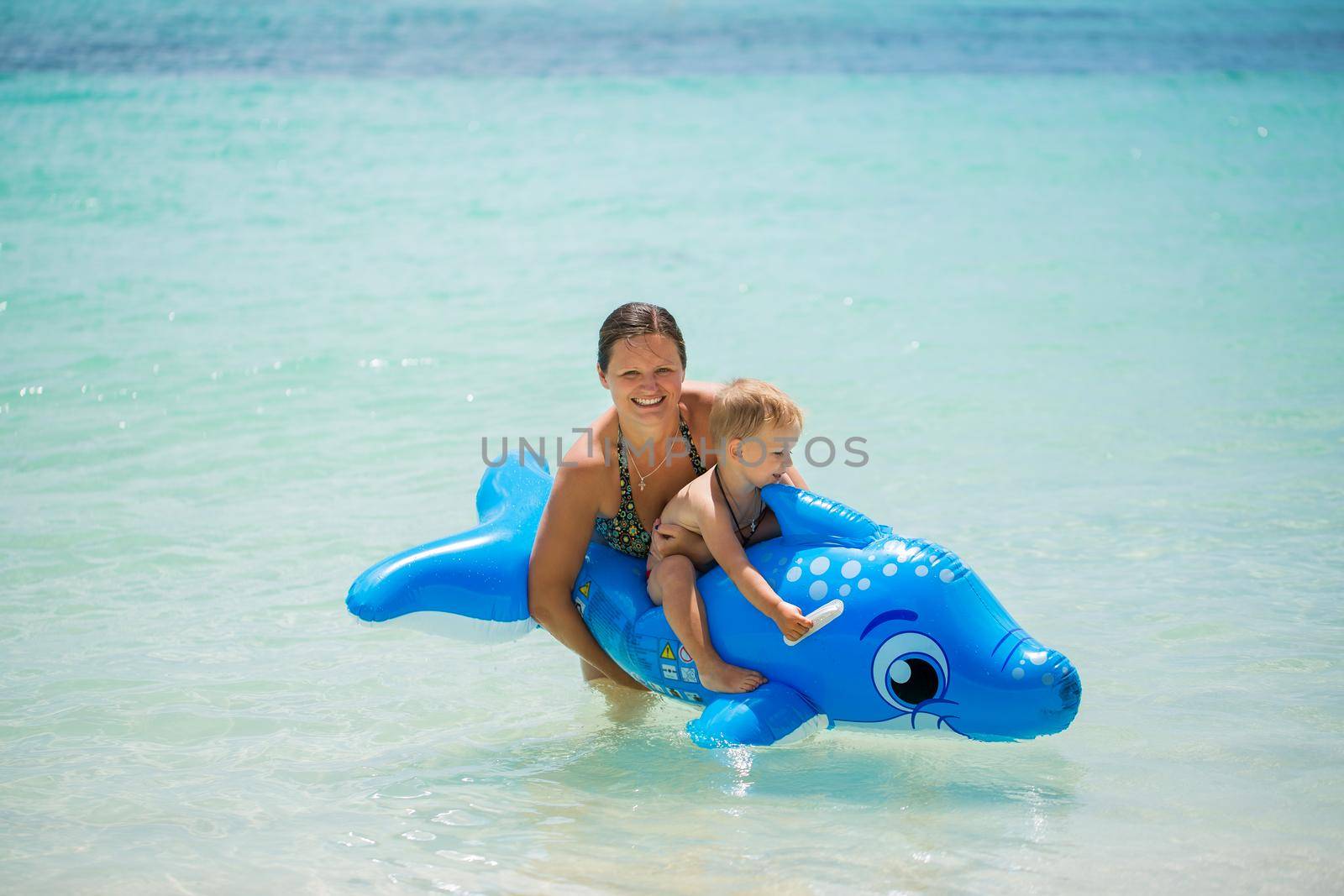 Mother and son swimming in the ocean on an inflatable Dolphin. by StudioPeace