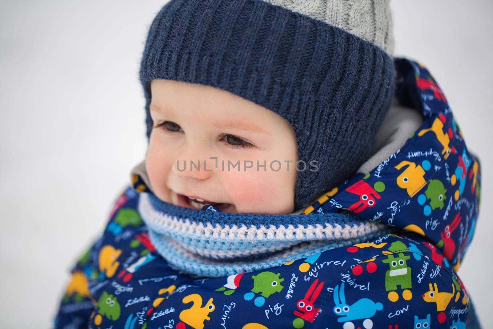 A little boy in a winter jacket is sitting in the snow