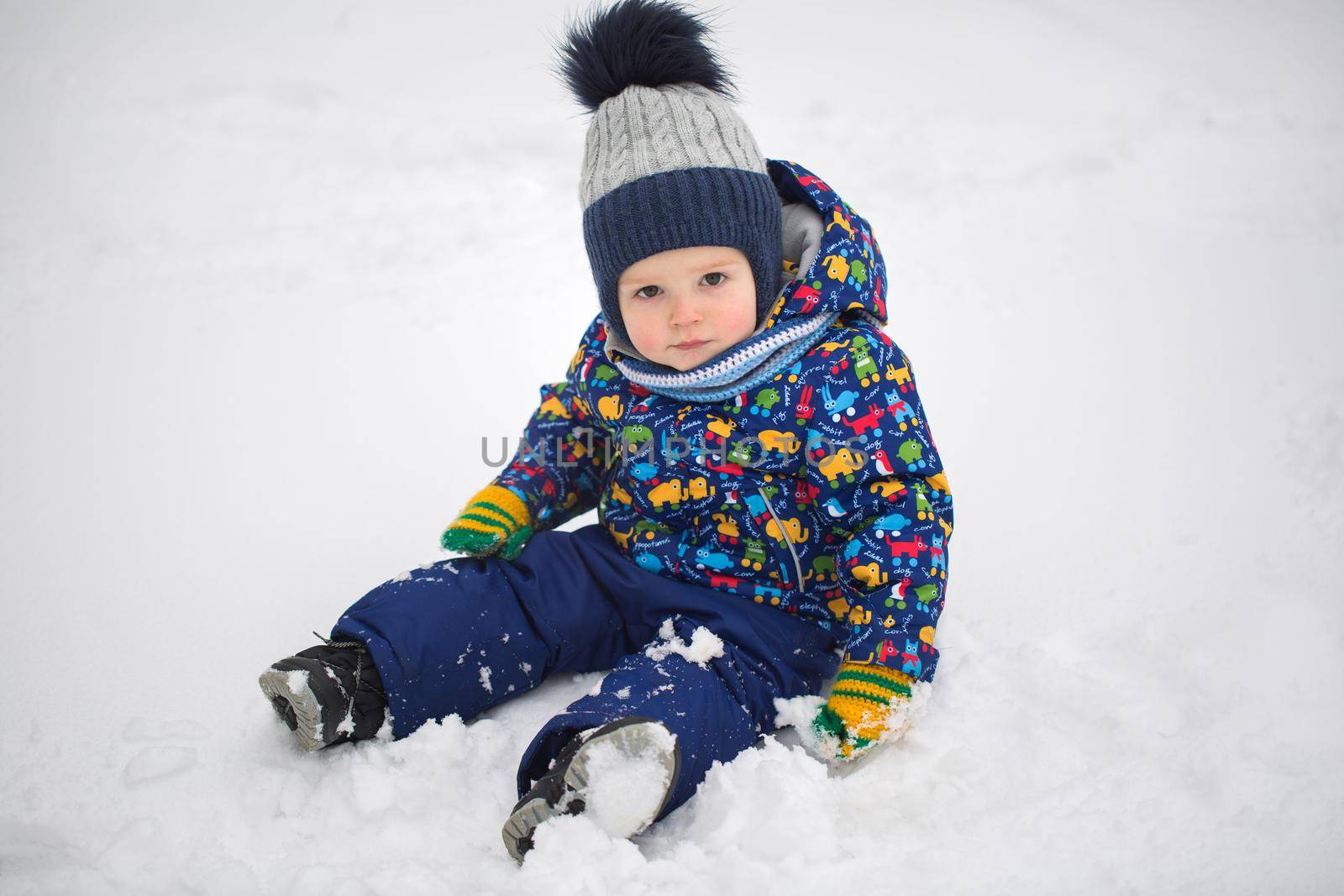 A little boy in a winter jacket is sitting in the snow