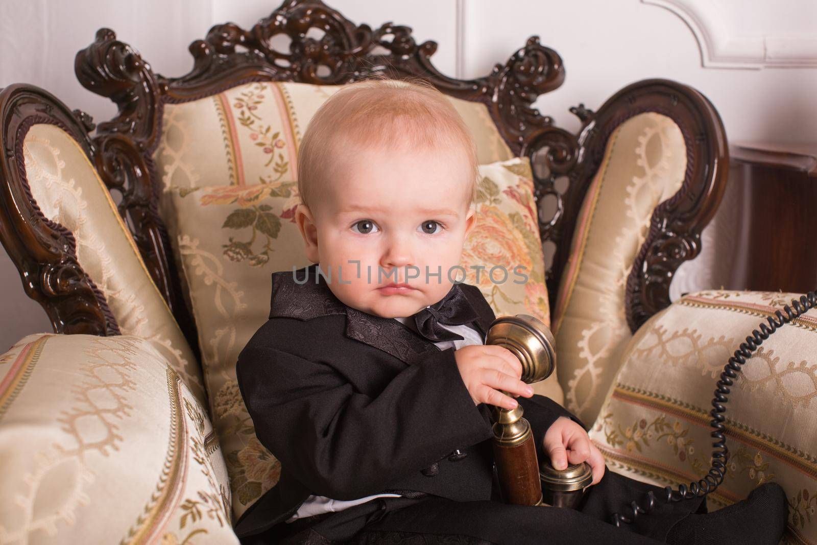Child in a tuxedo sitting in an office talking on the phone.