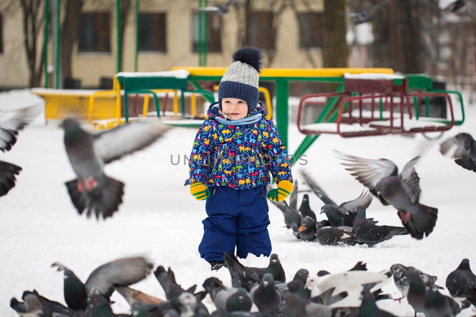 Little pretty boy feeds birds in winter snow park outdoor