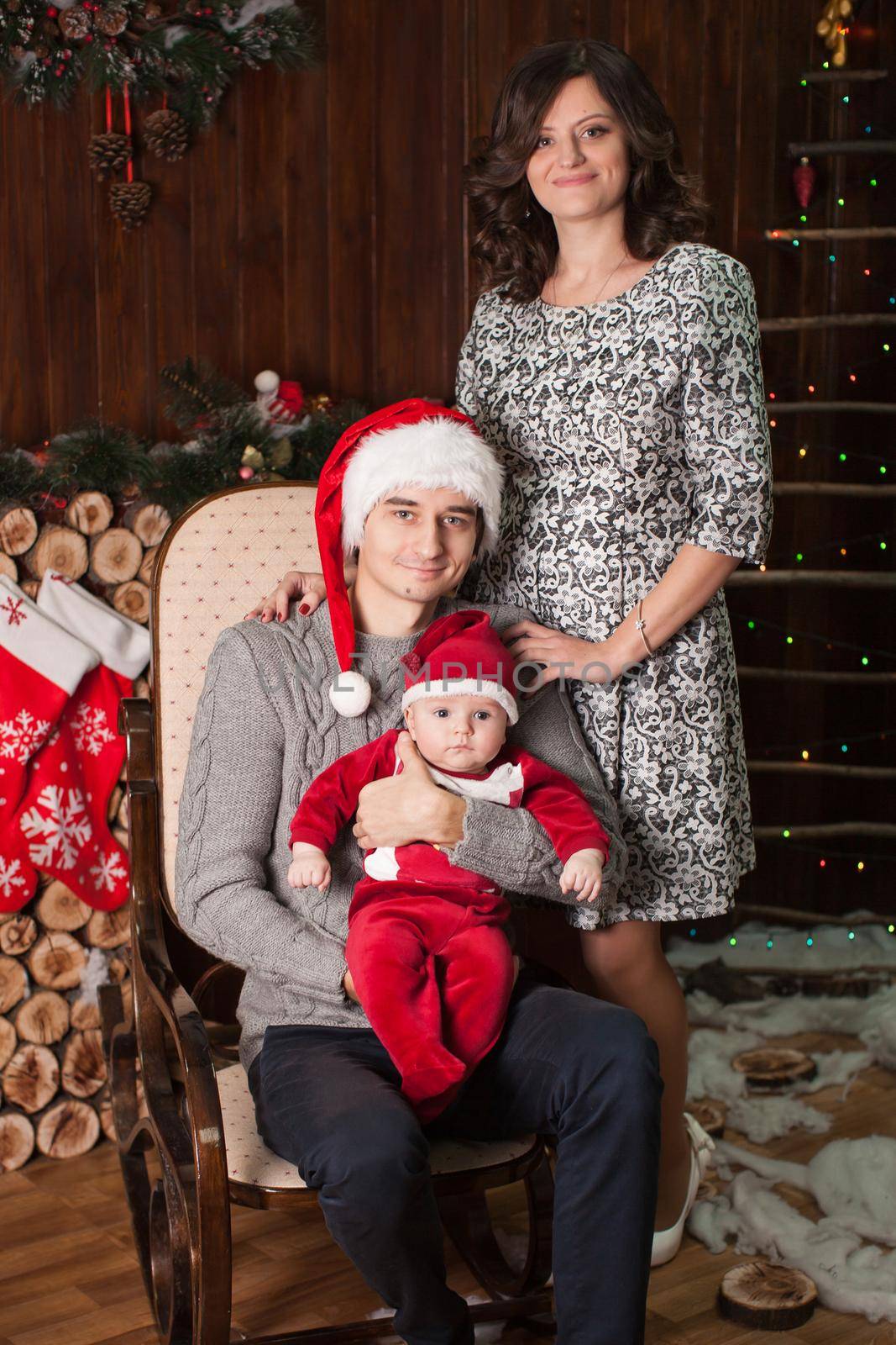 A family with a small child in Santa Claus costume at home in front of a fireplace on a rocking chair