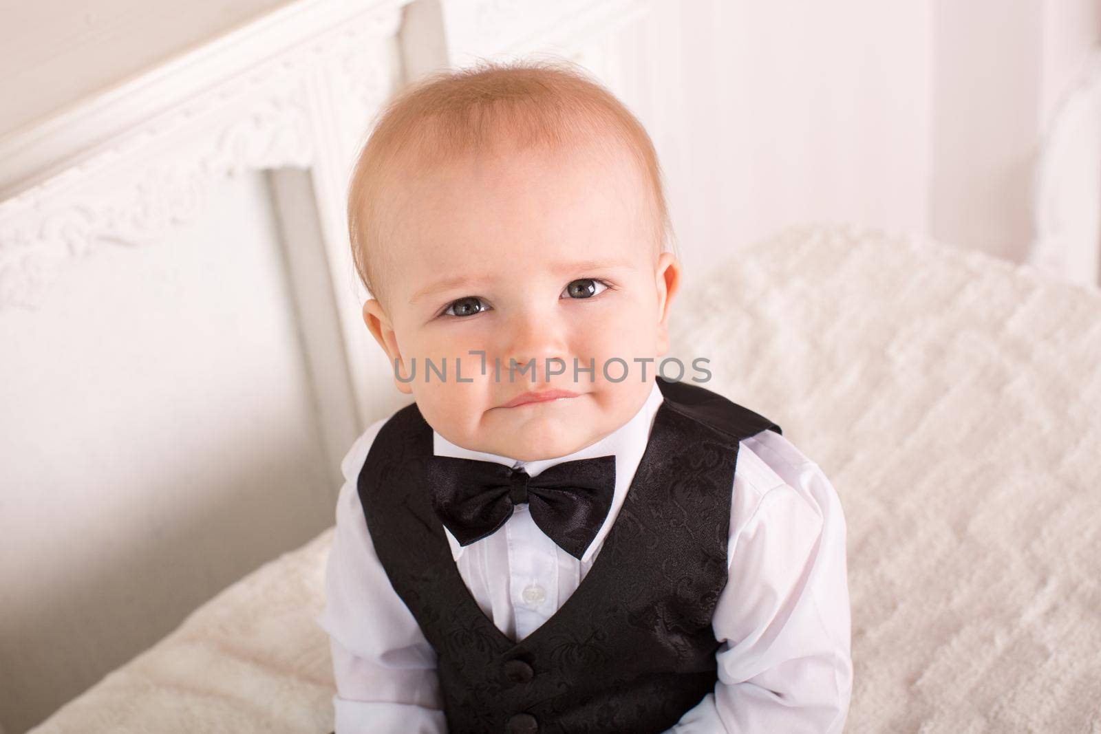 Child in a tuxedo, sitting on the bed next to the fireplace. The groom.