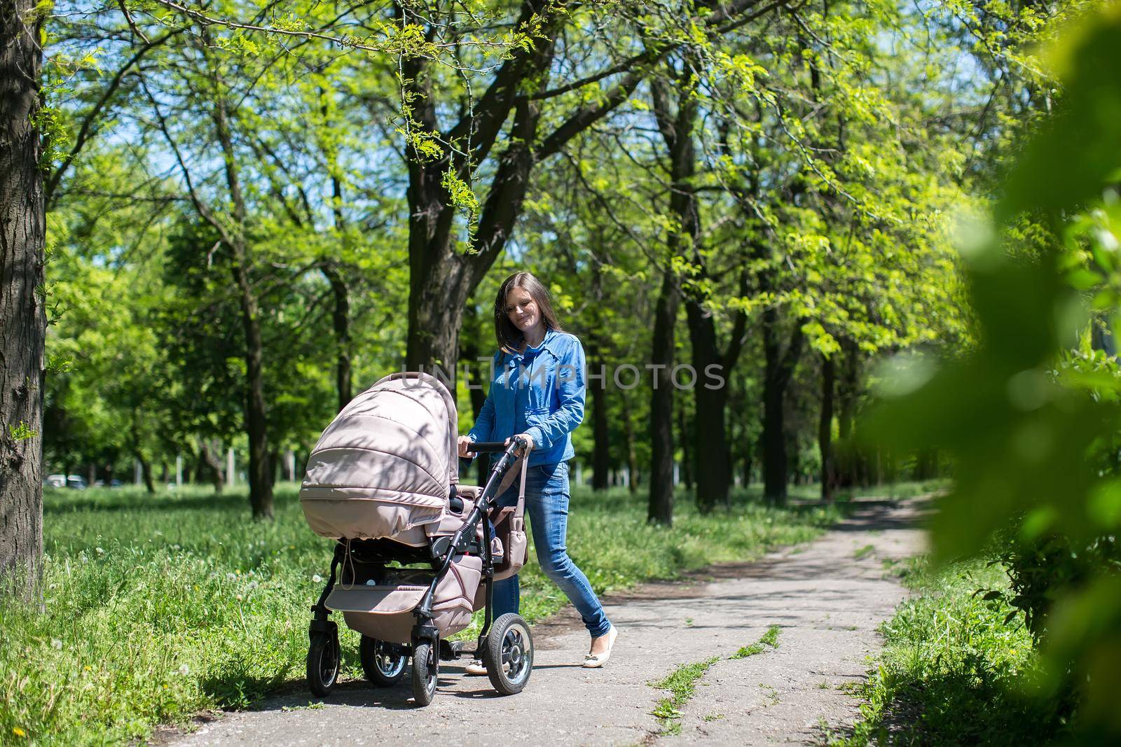 Young mother walking and pushing a stroller in the park. by StudioPeace