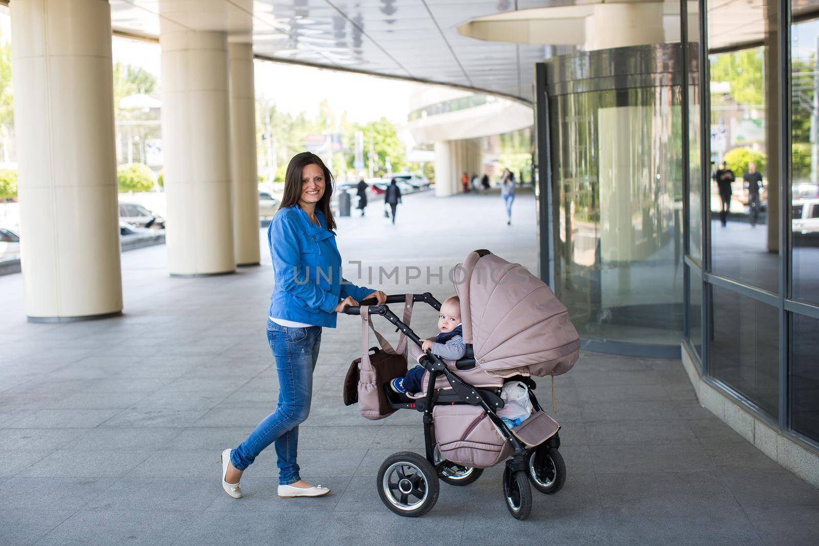Young mother walking and pushing a stroller. by StudioPeace