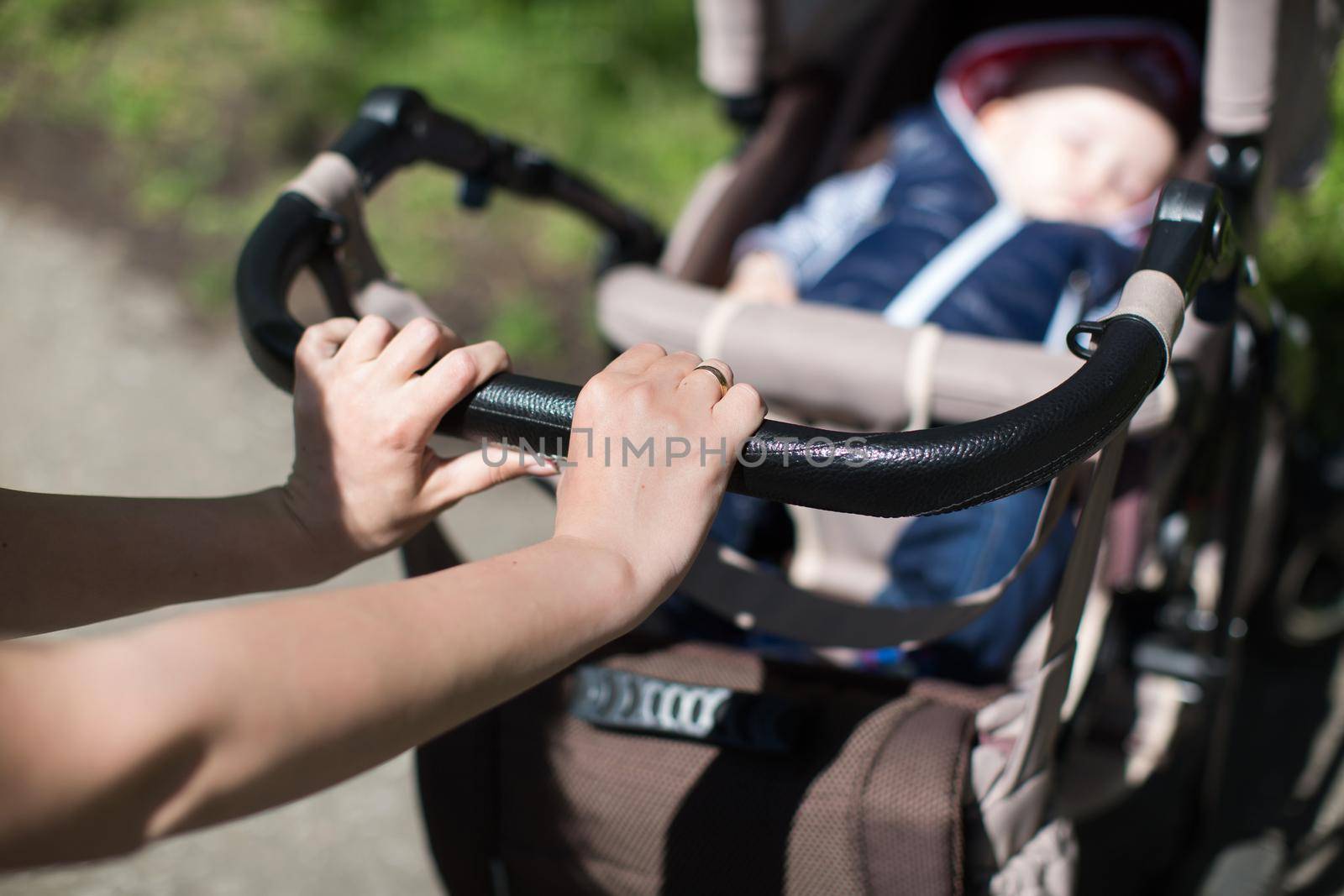 Young mother walking and pushing a stroller in the park. by StudioPeace