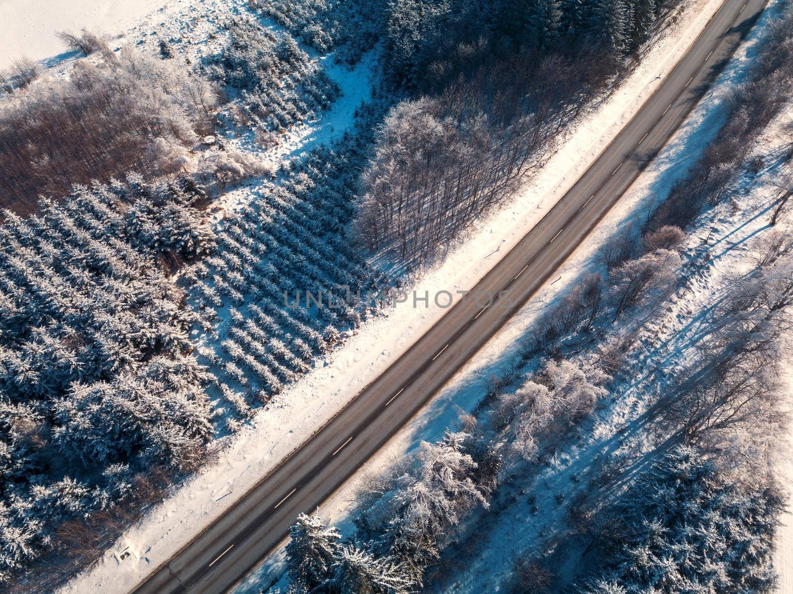 Aerial view of winter road, in sunny day. White frozen and snowy countryside landscape from bird eye, winter theme. Czech Republic, Vysocina region highland