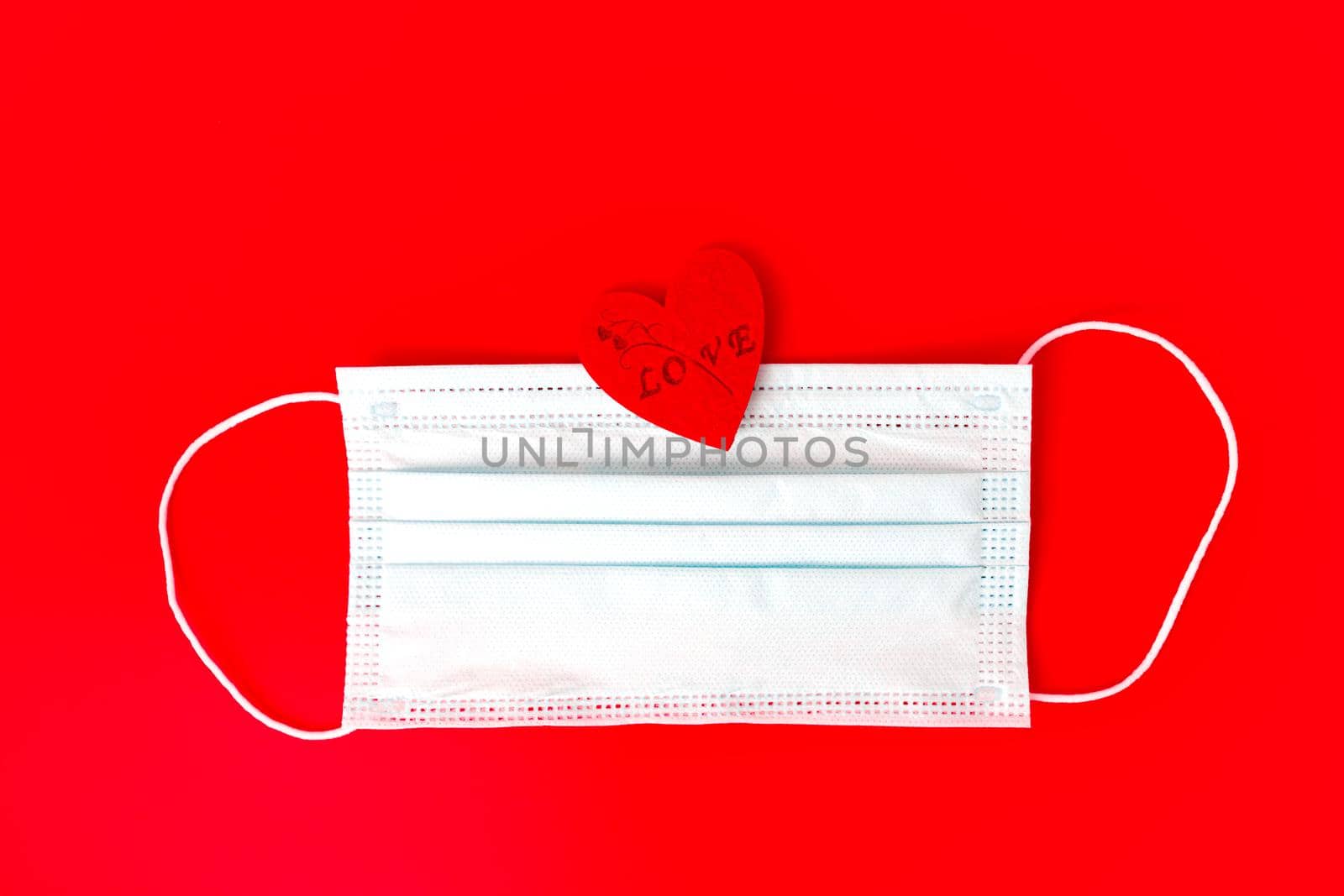 Medical face mask with red heart on red background . With copy space .Valentines day concept