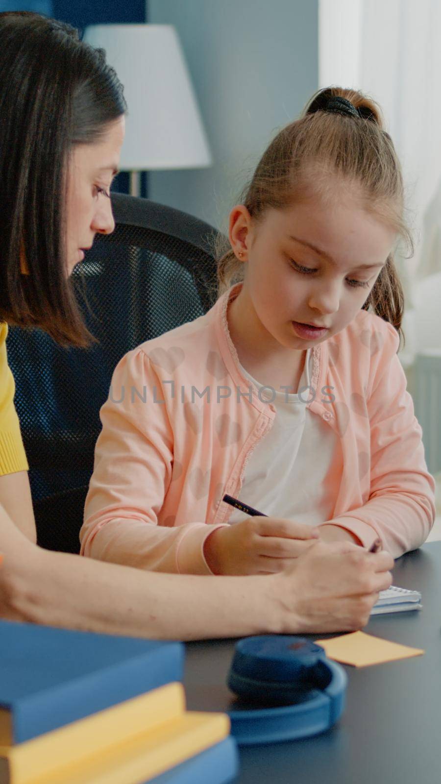 Mother and daughter doing homework together for online lesson on remote classroom. Parent helping little girl with school work and tasks for distance education on computer at home.