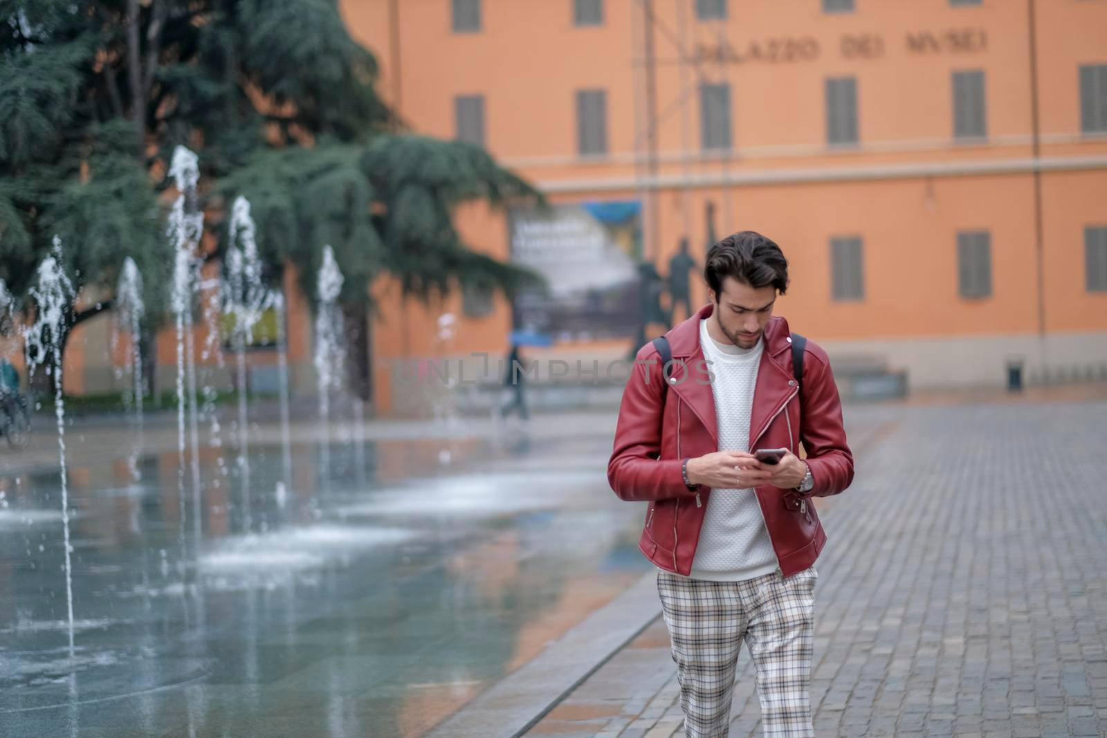 beautiful guy with red leather jacket and backpack in the center of reggio emilia. High quality photo