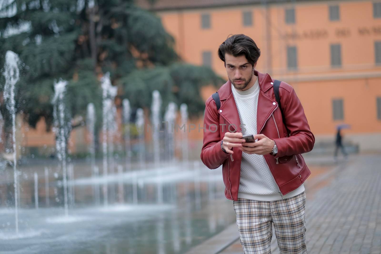 beautiful guy with red leather jacket and backpack in the center of reggio emilia. High quality photo