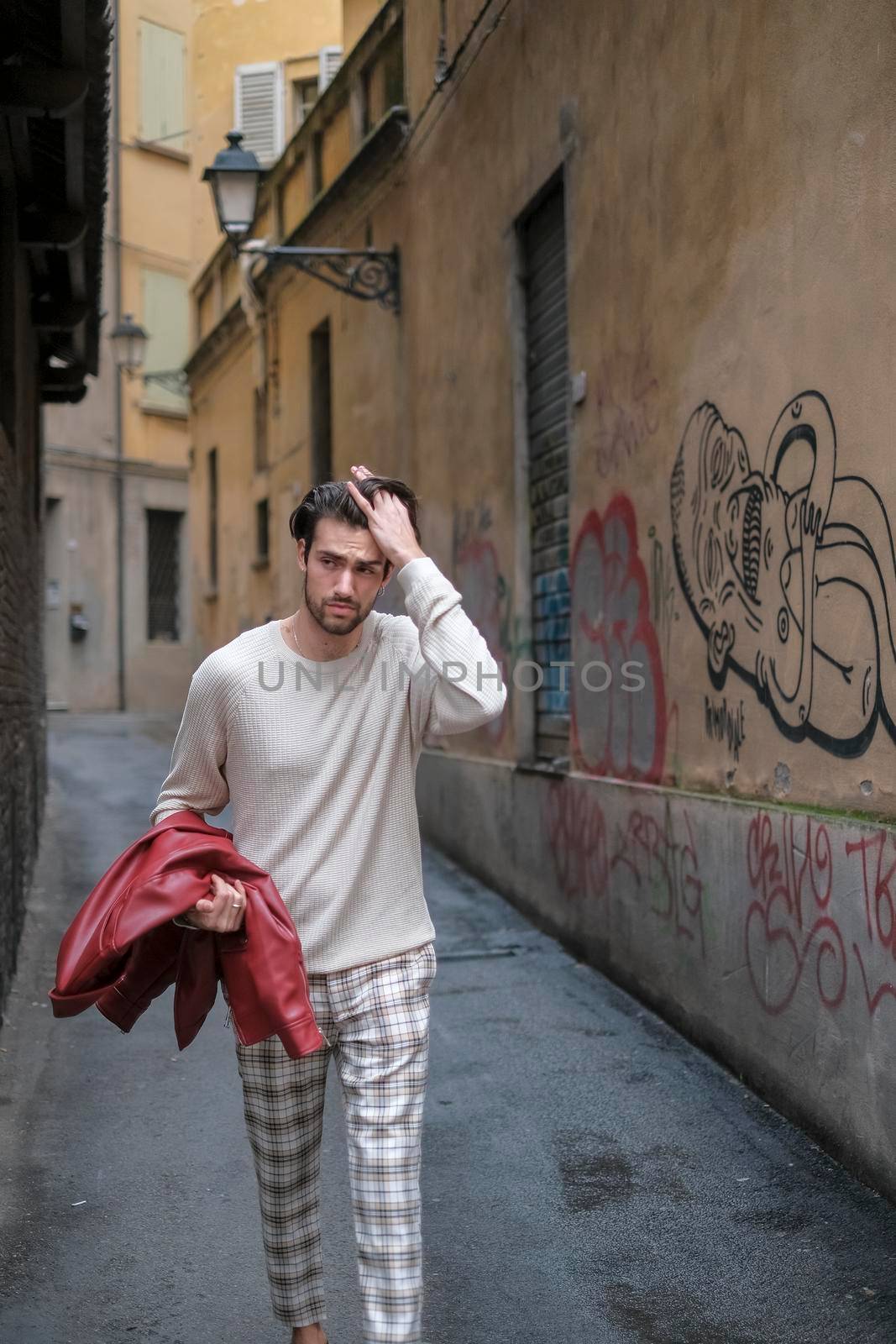 beautiful guy with red leather jacket and backpack in the center of reggio emilia. High quality photo