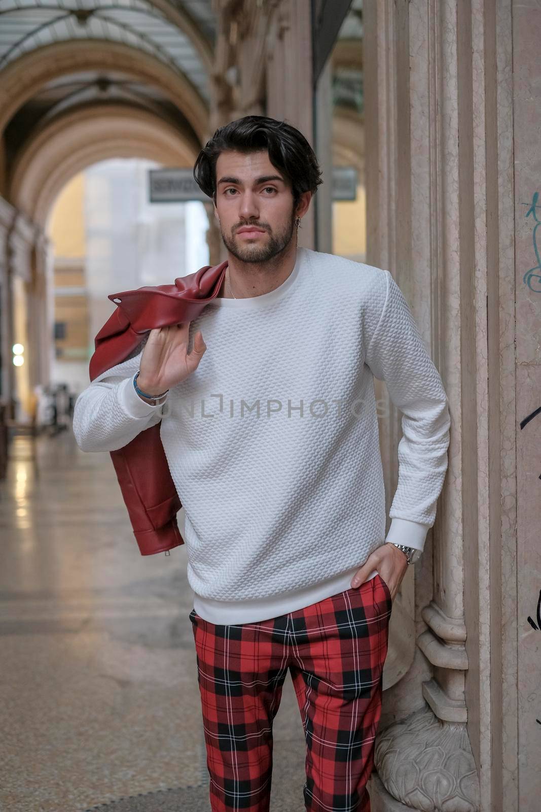 beautiful guy with red leather jacket and backpack in the center of reggio emilia. High quality photo