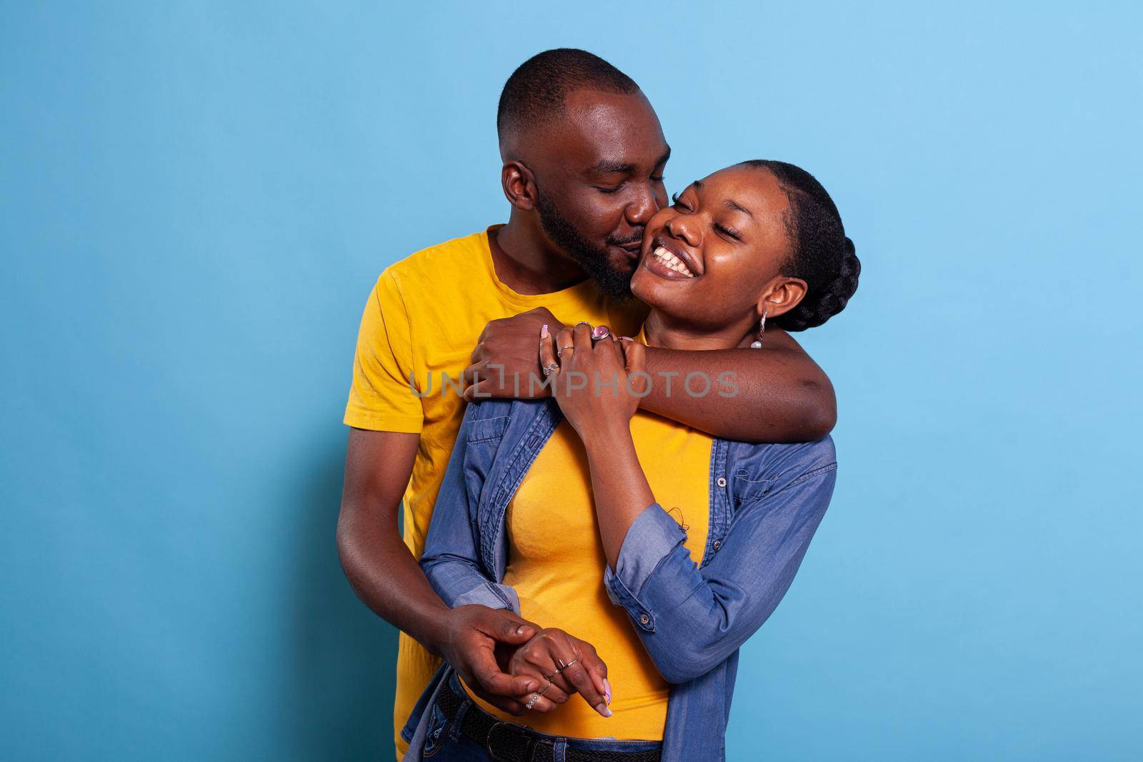 African american couple smiling and hugging each other over blue background. Man and woman in relationship expressing tenderness and affection, sharing embrace together. Cheerful people