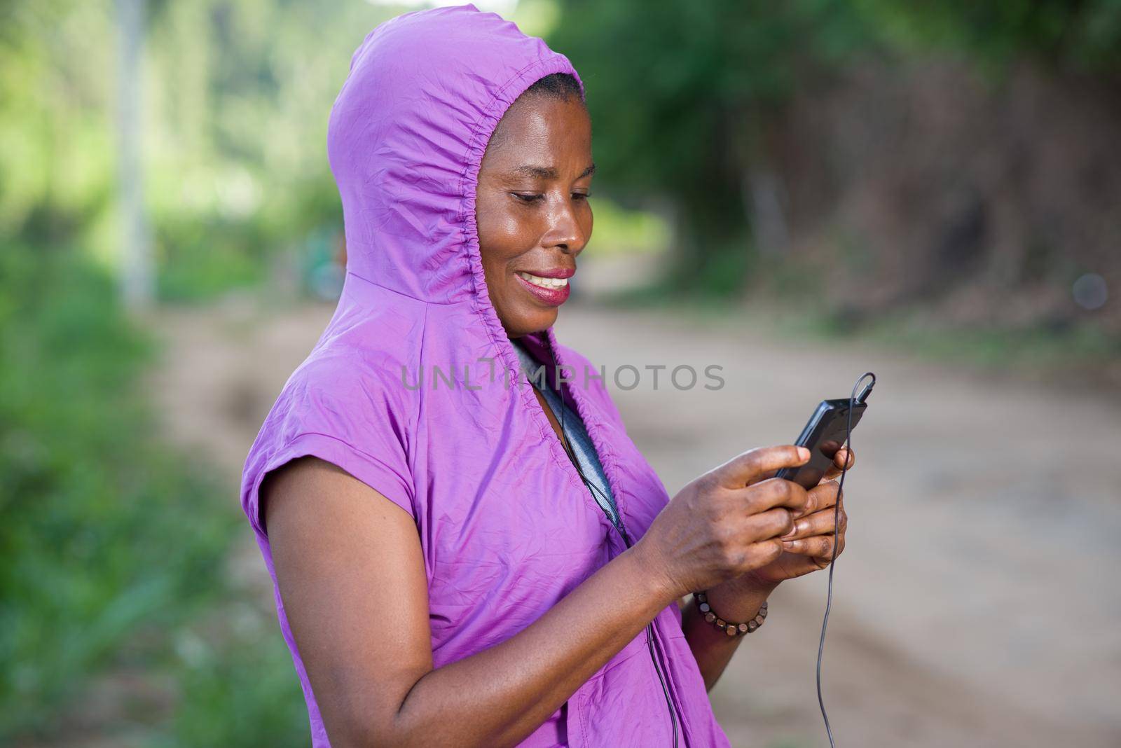 young woman standing in purple dress looking at her mobile phone while smiling.