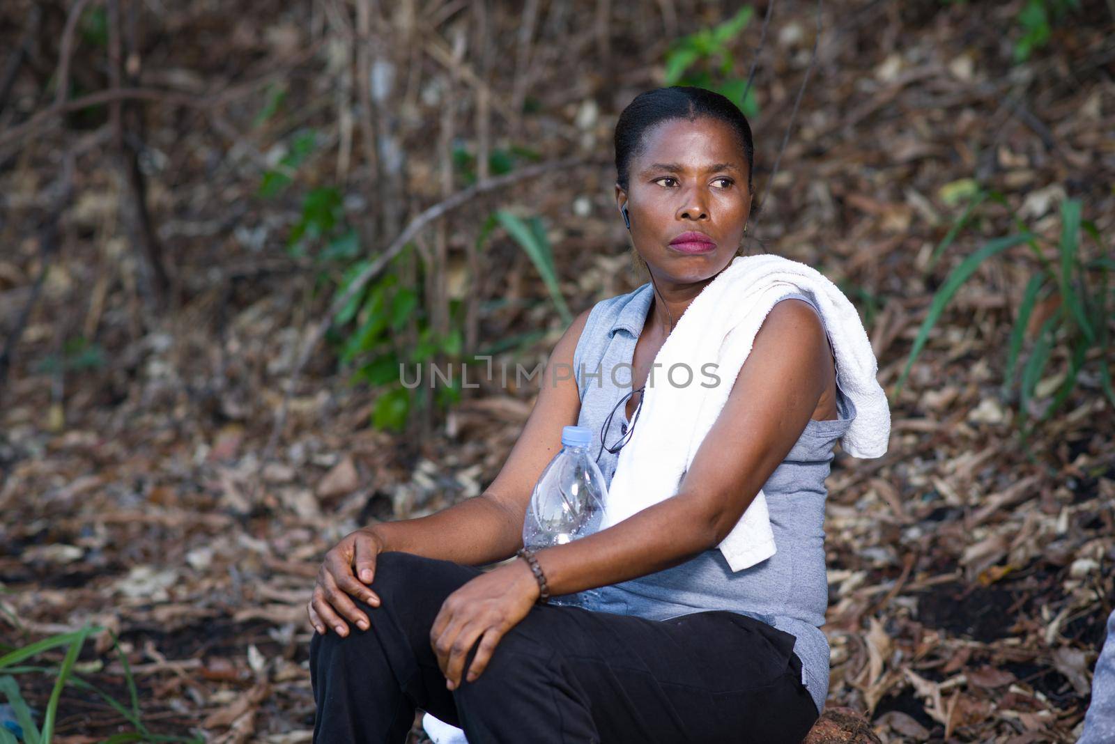 young woman in sportswear sitting on a piece of wood listening to music while watching the camera.