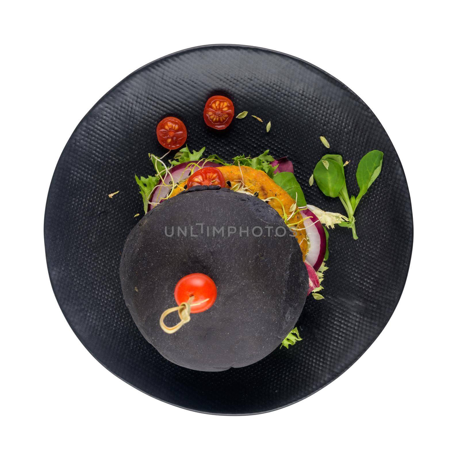 Tasty grilled veggie burger with chickpeas and vegetables and black bread on black ceramic plate isolated on white background.