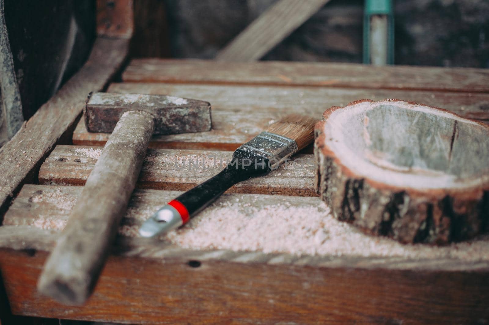 an old rusty hammer, a paint brush and a round pine beam with sawdust on a bench. Wooden stand for food for the master class. DIY concept.