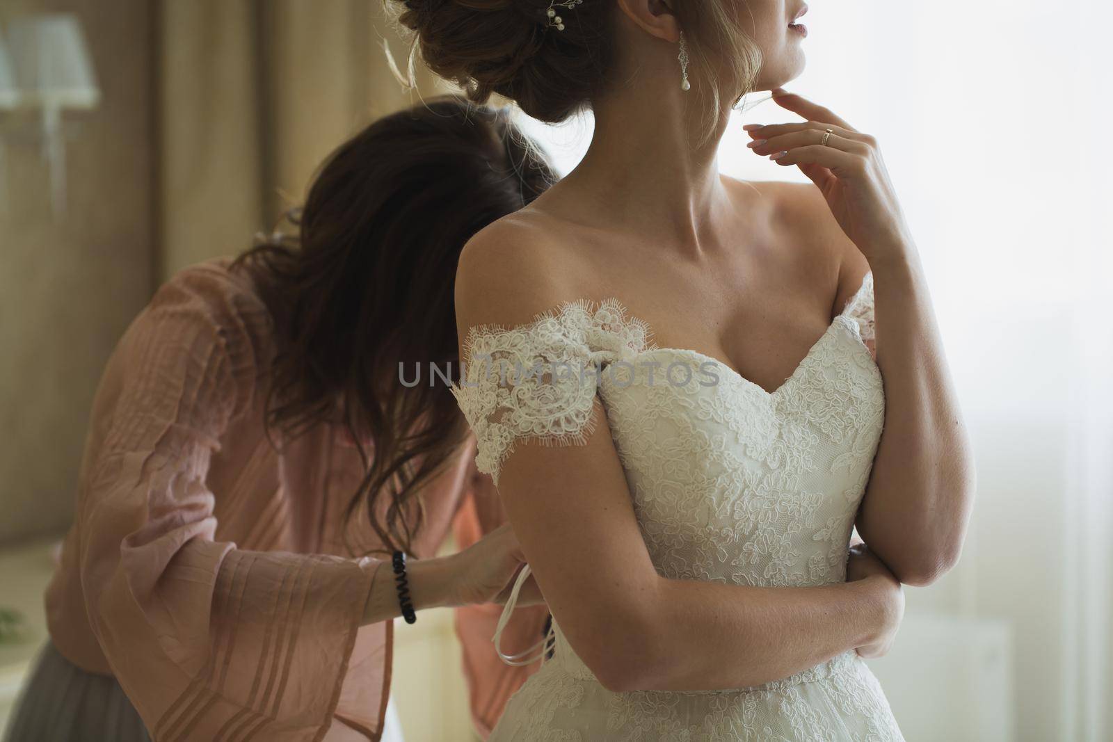 Bridesmaid is helping the bride to dress. by StudioPeace