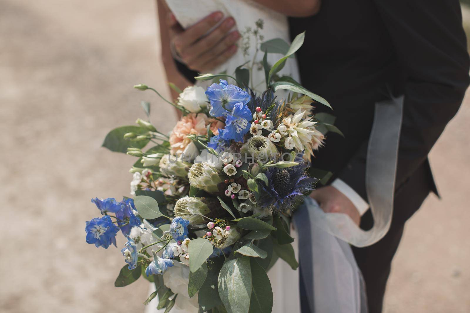 The hand of the groom hugging the back of the bride. Wedding bouquet in the foreground.