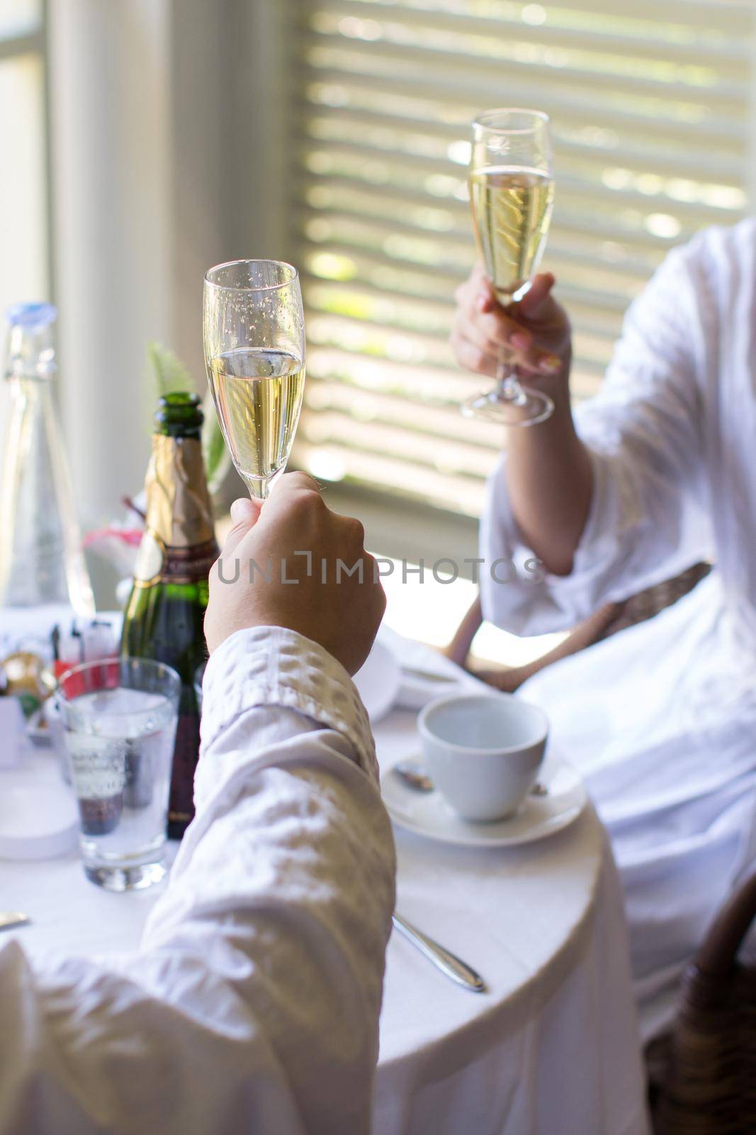 A couple in dressing gowns in a hotel drinking champagne by StudioPeace