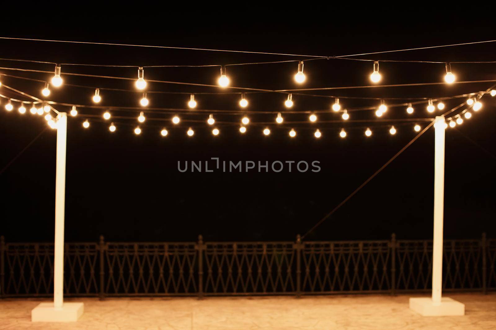 Garlands of lamps on a wooden stand on the street. A wedding Banquet by StudioPeace