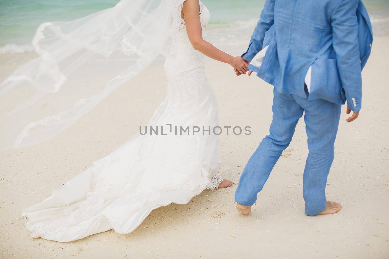 Beautiful gorgeous bride and stylish groom holding hands, on the background of a sea. by StudioPeace