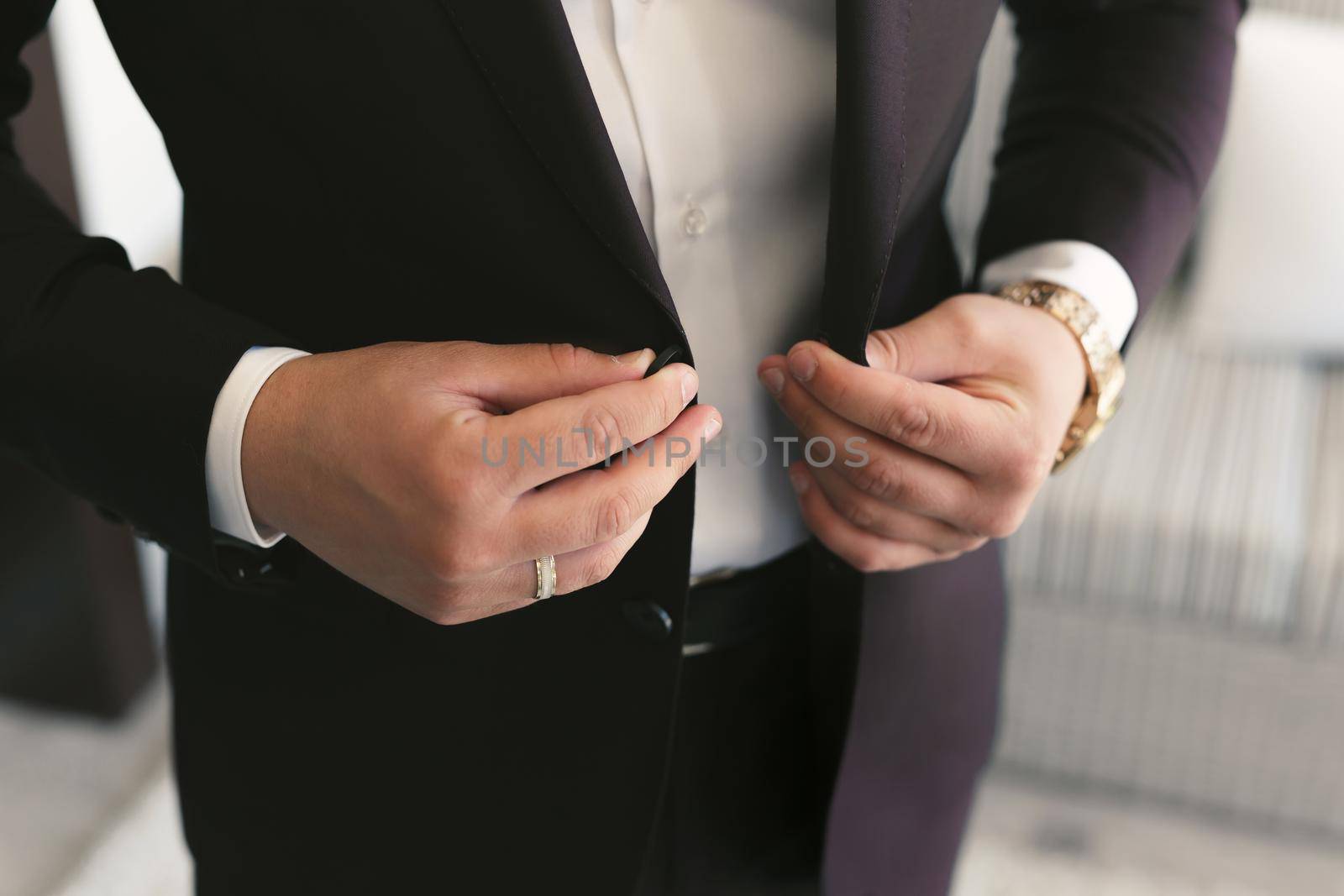 A man puts on a wedding suit and fastens a button by StudioPeace