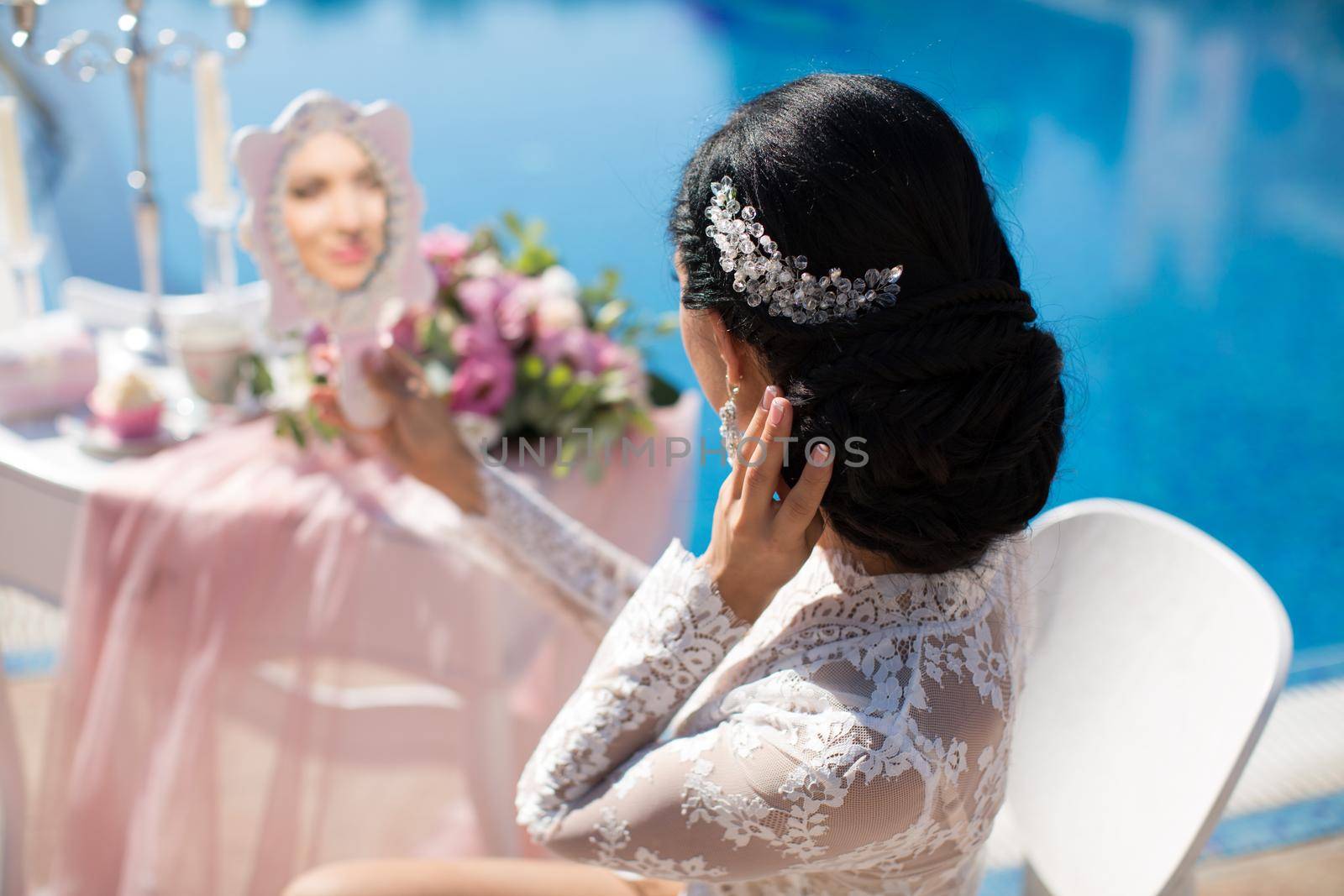 Bride adjusts her hair and looks in the mirror at the pool at the hotel by StudioPeace