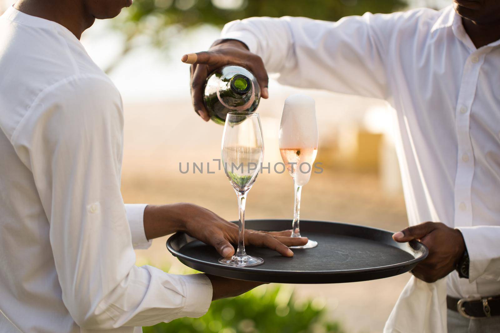 The waiter pours champagne into the glasses that are on the tray. by StudioPeace