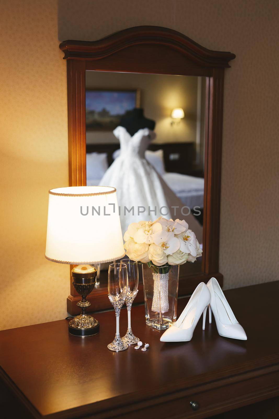 Wedding dress on a mannequin is reflected in the mirror against the background of shoes, bouquet and glasses