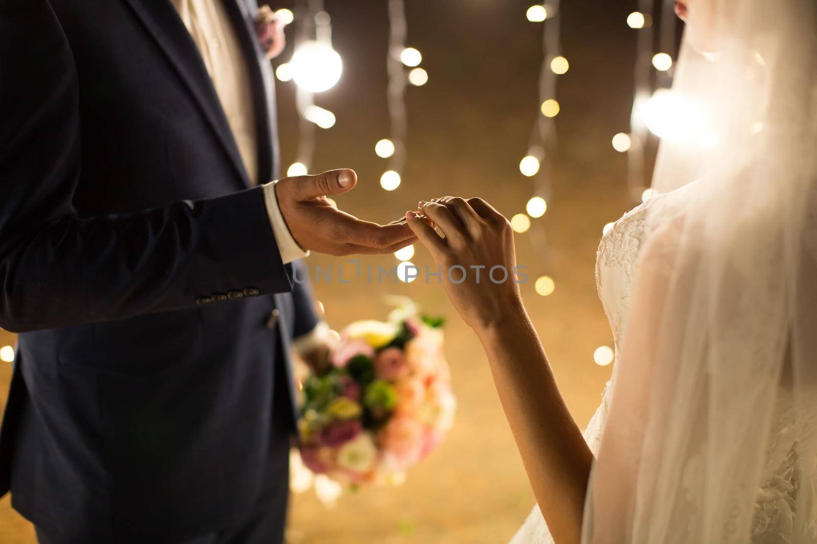 Evening wedding ceremony. The bride and groom holding hands on a background of lights and lanterns.