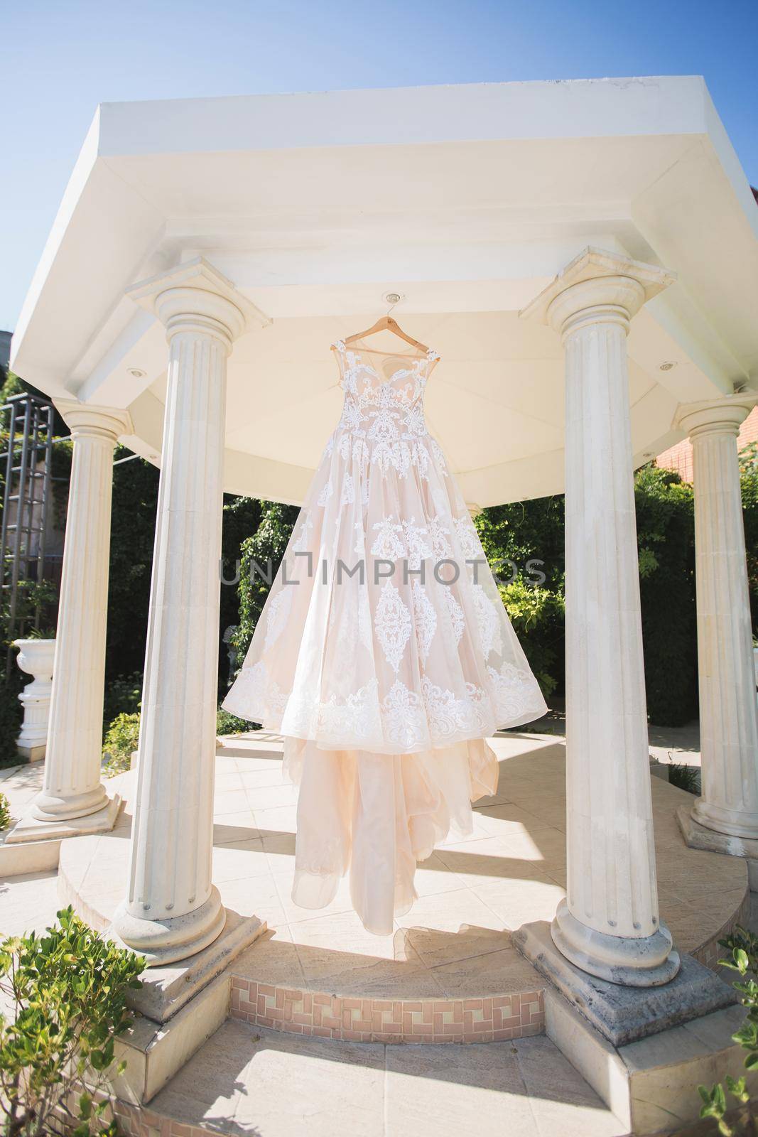 The wedding dress is hanging in a beautiful white gazebo.