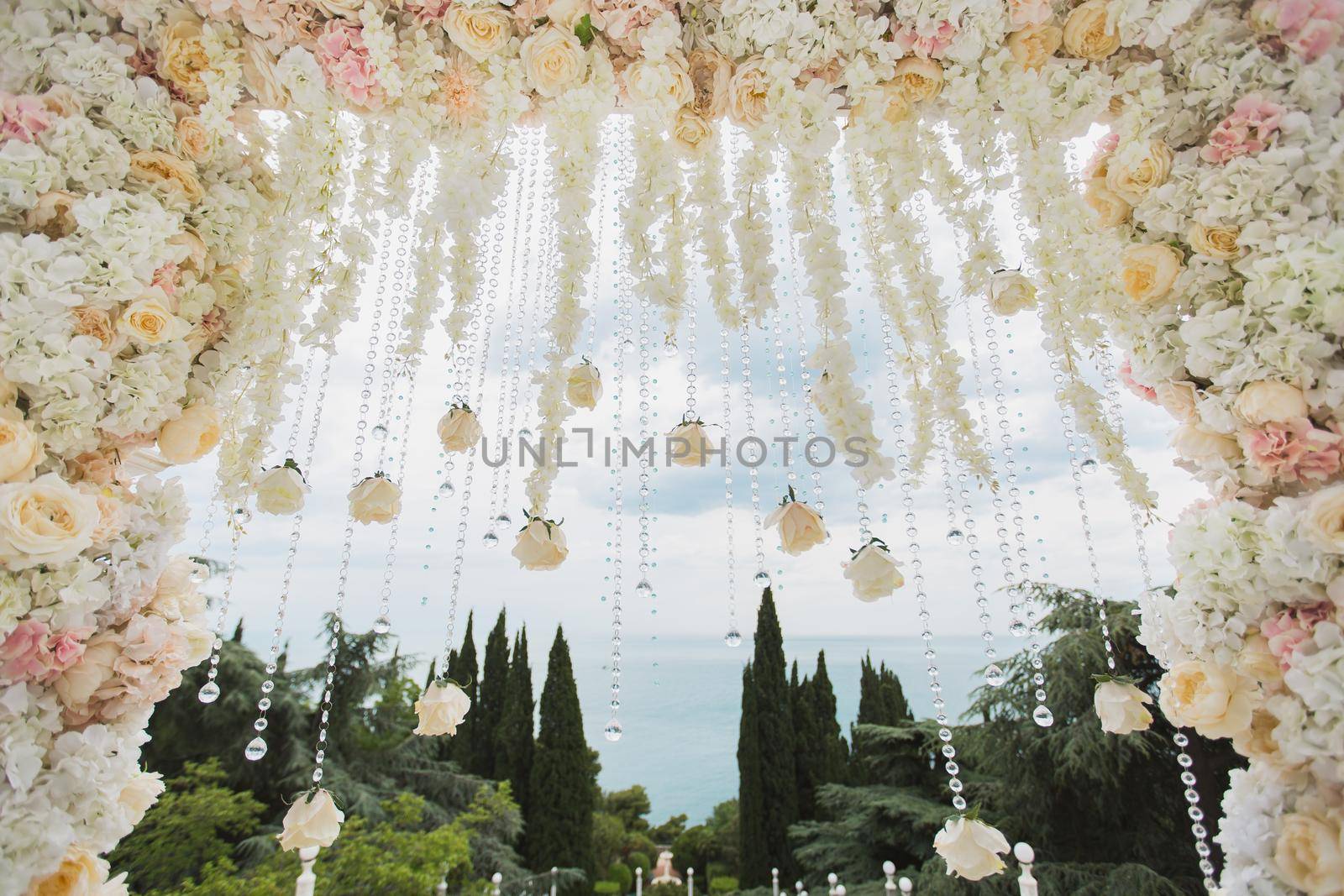 Wedding arch with flowers and beads on blue sky background close-up.