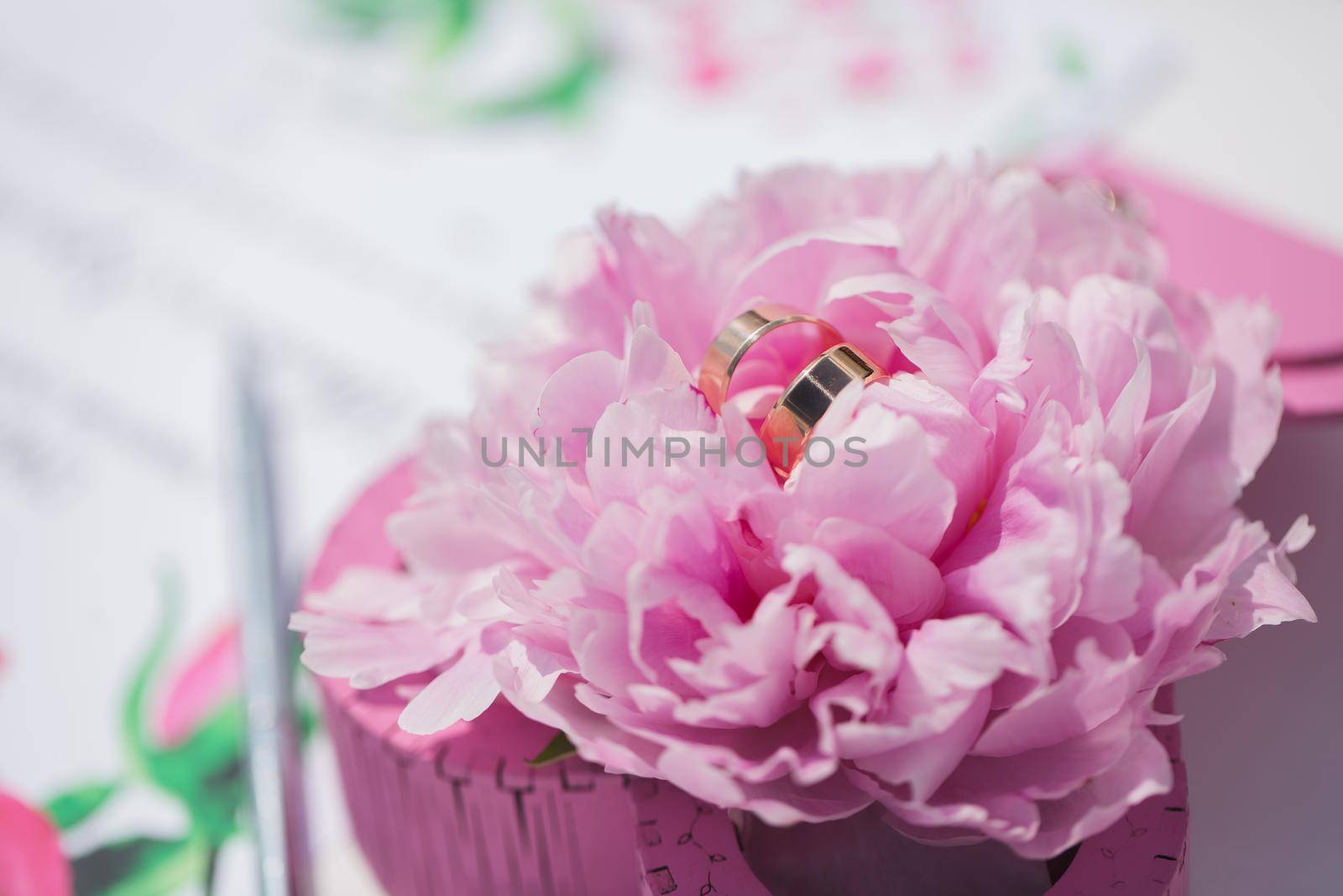 Gold wedding rings on a background of flowers peony. Wedding card with flowers peony closeup by StudioPeace