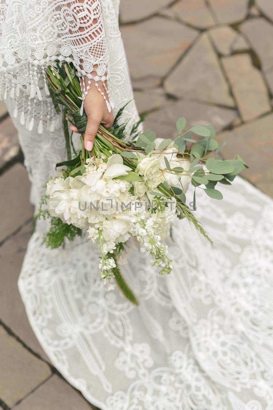 Delicate bouquet of white peonies in the hands of the bride on the background of the train of the wedding dress.