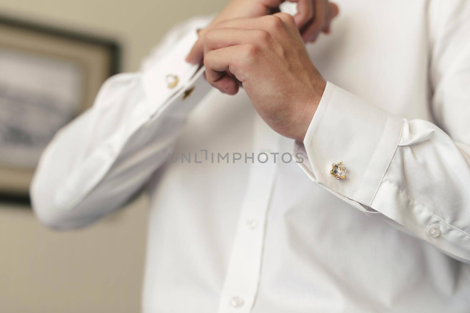 Men put on a shirt and fasten cufflinks on the morning of the wedding day by StudioPeace