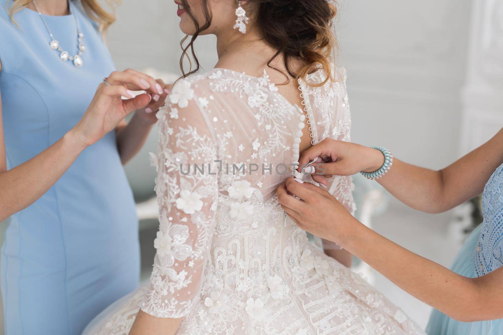 Female hands button the wedding dress to the bride with a beautiful hairstyle