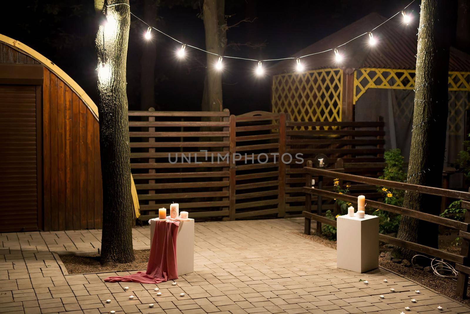 Garden with a wooden gazebo with lights, candles at night at a wedding. by StudioPeace