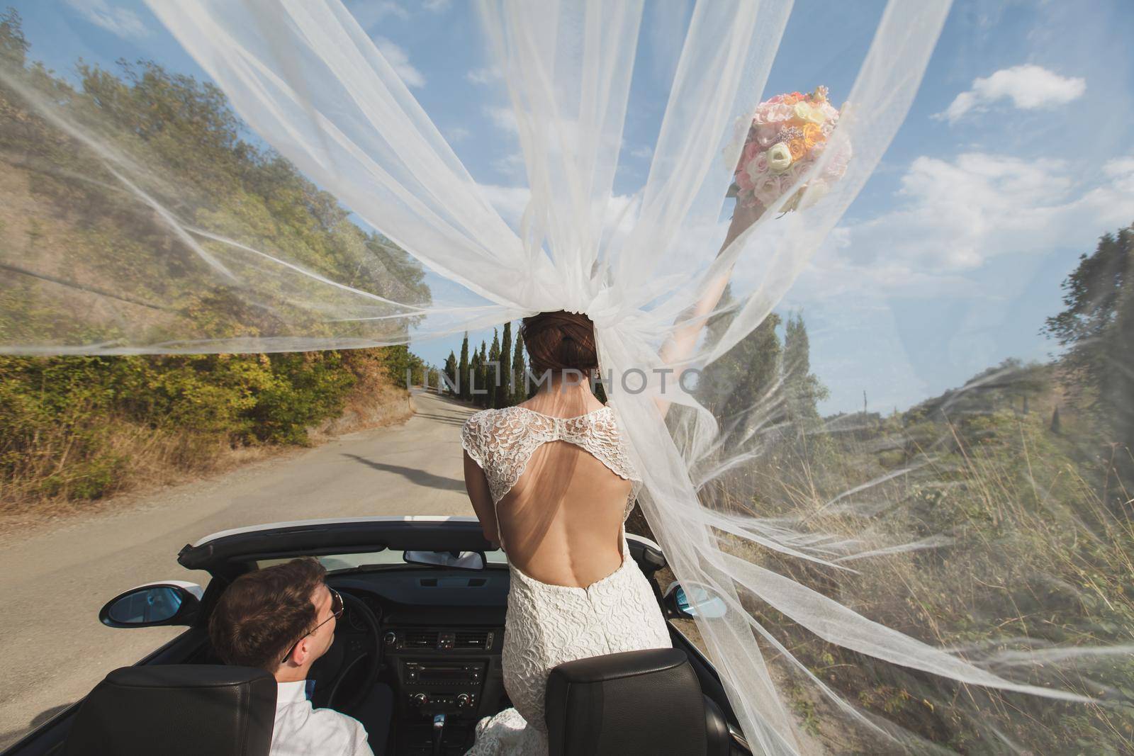 Beautiful stylish young successful couple enjoying riding in the car at wedding walk in the tropical country or island. by StudioPeace