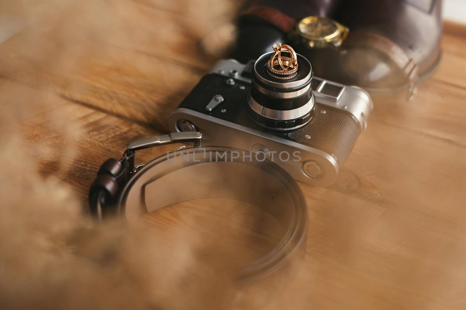 Wedding rings on an old camera, shoes, watch, and belt. Men's attributes on the wooden floor