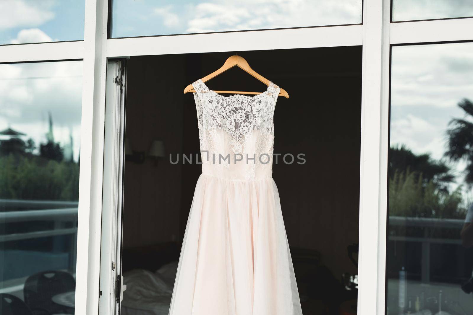 Luxurious peach wedding dress hangs on a chandelier in a white room. by StudioPeace