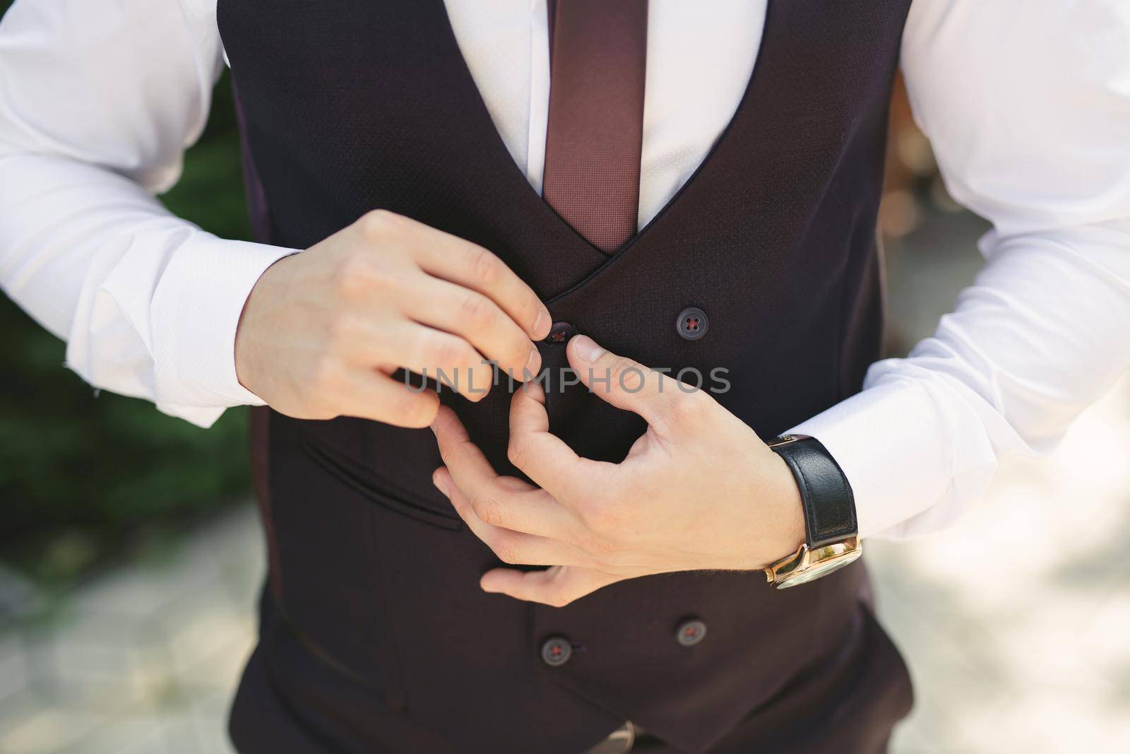 A man puts on a wedding suit and fastens a button.